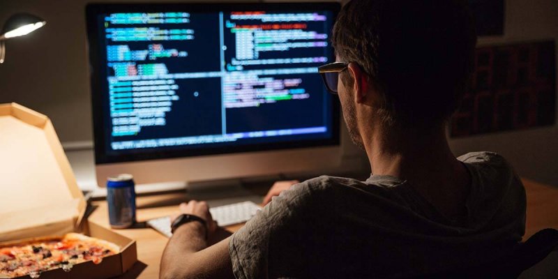 Back view of focused programmer writing code and eating pizza